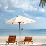 two brown wooden armchairs beside umbrella near seashore